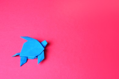 Origami art. Handmade light blue paper turtle on pink background, top view with space for text