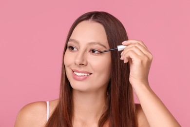 Beautiful woman applying serum onto hair on pink background