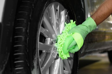 Photo of Worker washing car wheel with sponge, closeup