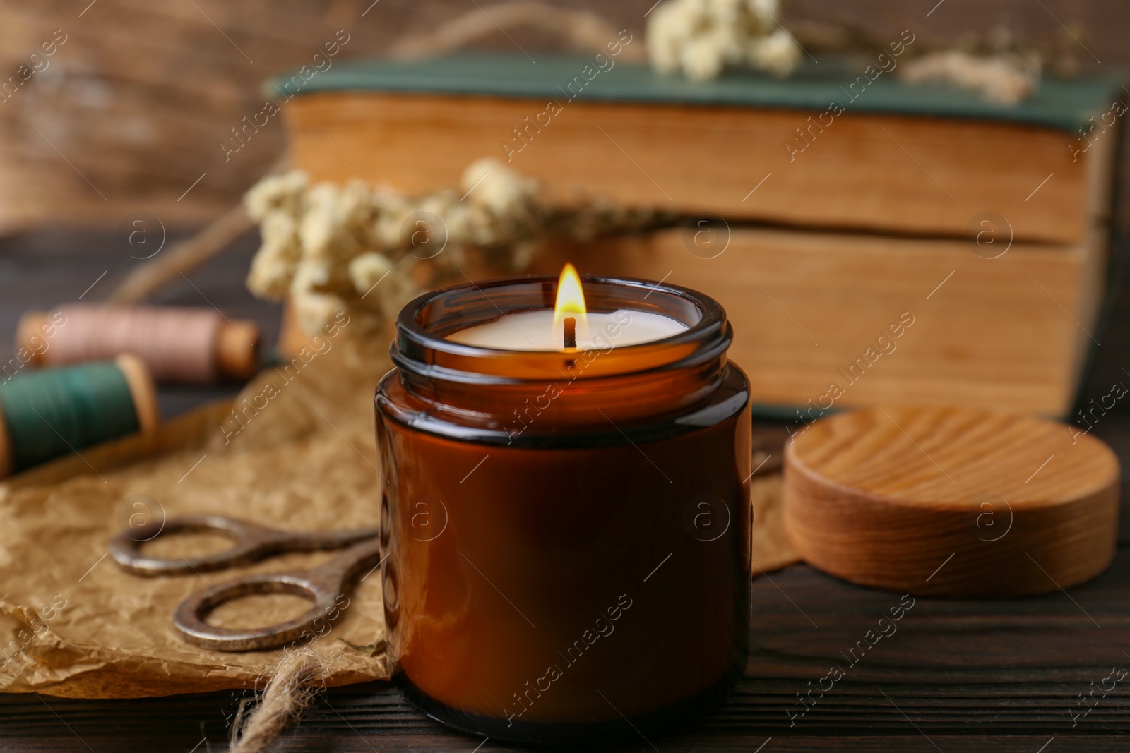 Photo of Burning scented candle, book and flowers on wooden table, closeup