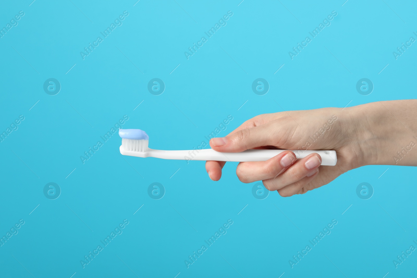 Photo of Woman holding toothbrush with paste on light blue background, closeup