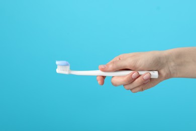 Photo of Woman holding toothbrush with paste on light blue background, closeup