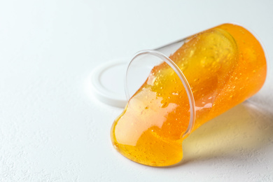 Overturned plastic container with orange slime on white background, closeup. Space for text