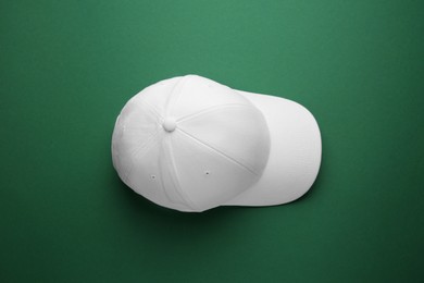 Photo of Stylish white baseball cap on green background, top view