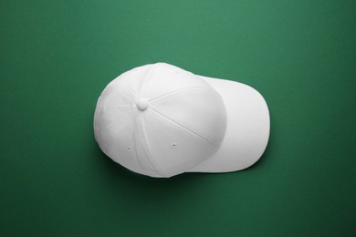 Stylish white baseball cap on green background, top view