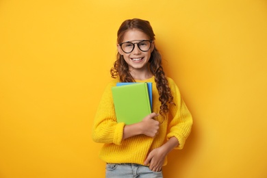 Photo of Cute little girl with glasses and books on yellow background. Reading concept