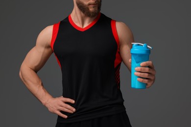 Young man with muscular body holding shaker of protein on grey background, closeup