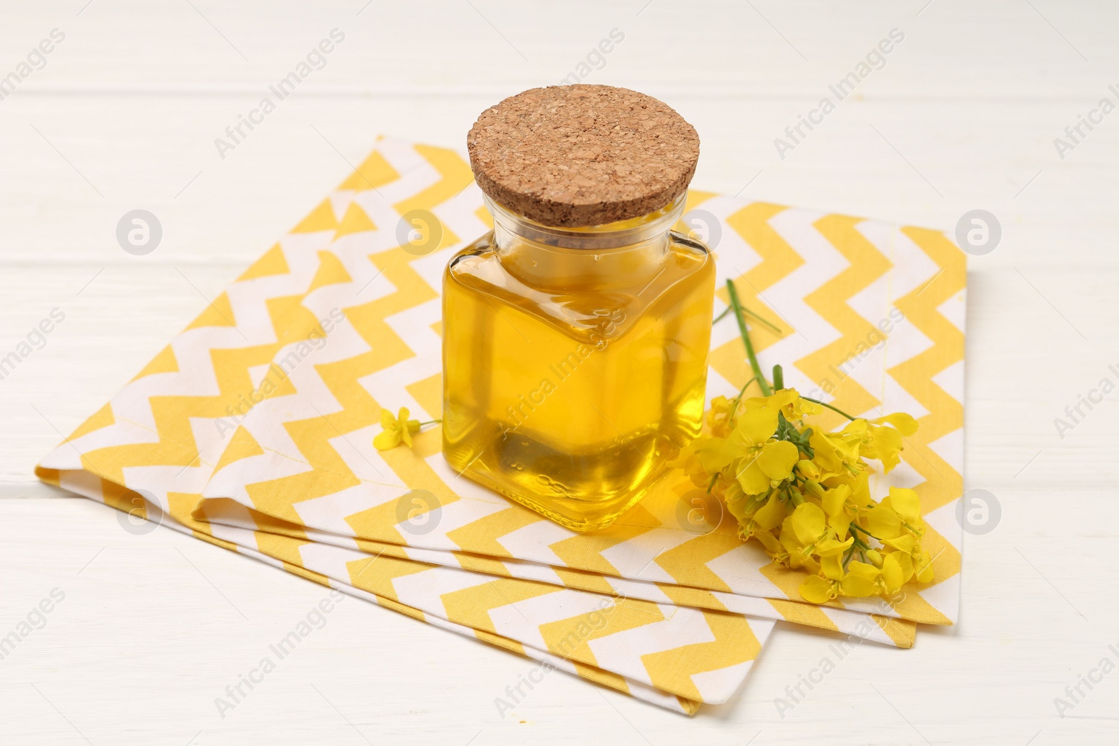 Photo of Rapeseed oil in glass bottle and beautiful yellow flowers on white wooden table
