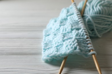 Knitting, soft turquoise yarn and needles on white wooden table, closeup