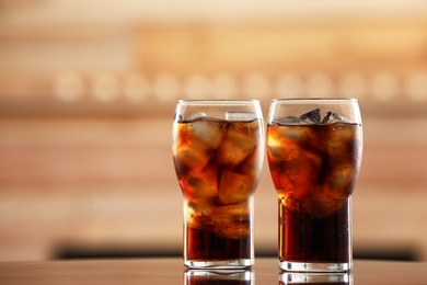 Photo of Glasses of cola with ice on table against blurred background. Space for text