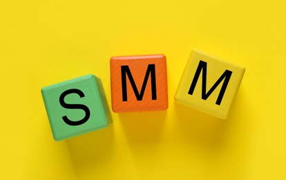 Photo of Colorful cubes with abbreviation SMM (Social media marketing) on yellow background, flat lay