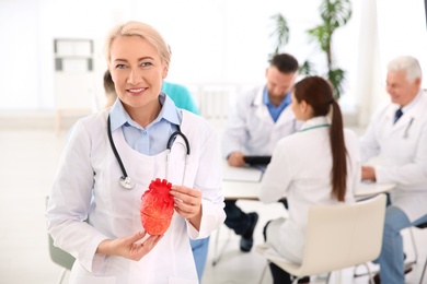 Photo of Female doctor holding heart model in clinic. Cardiology center