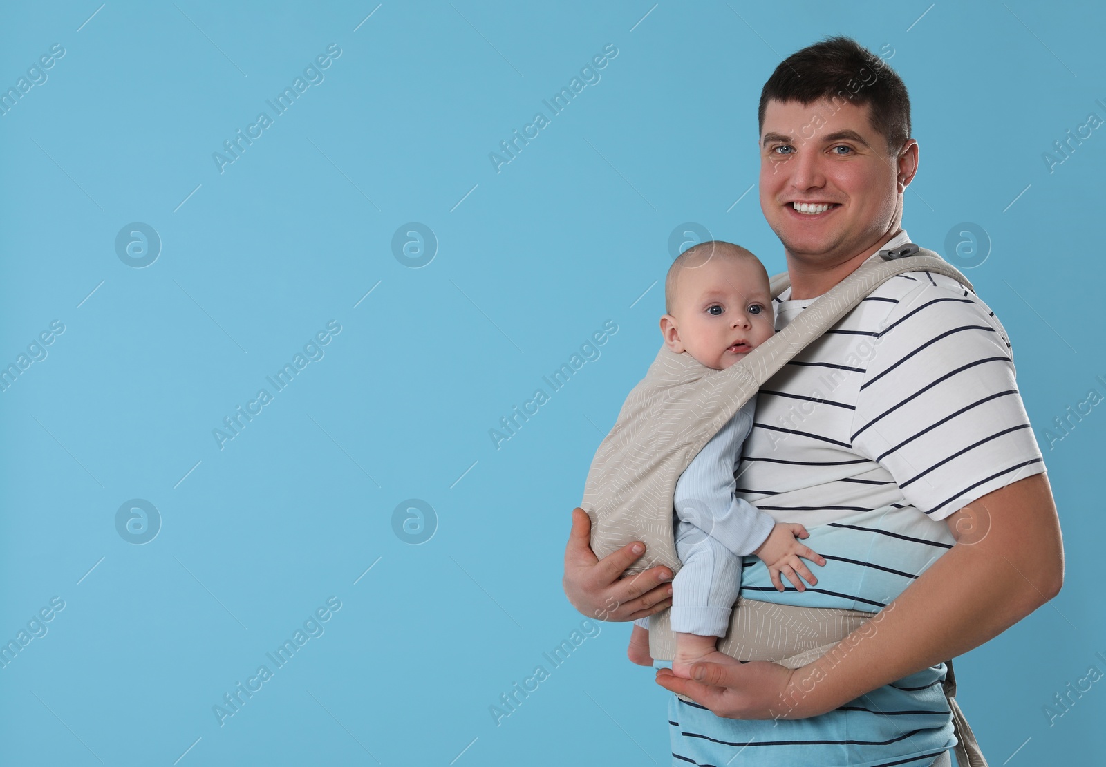 Photo of Father holding his child in sling (baby carrier) on light blue background. Space for text