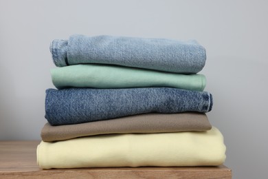 Stack of different folded clothes on wooden table near grey wall