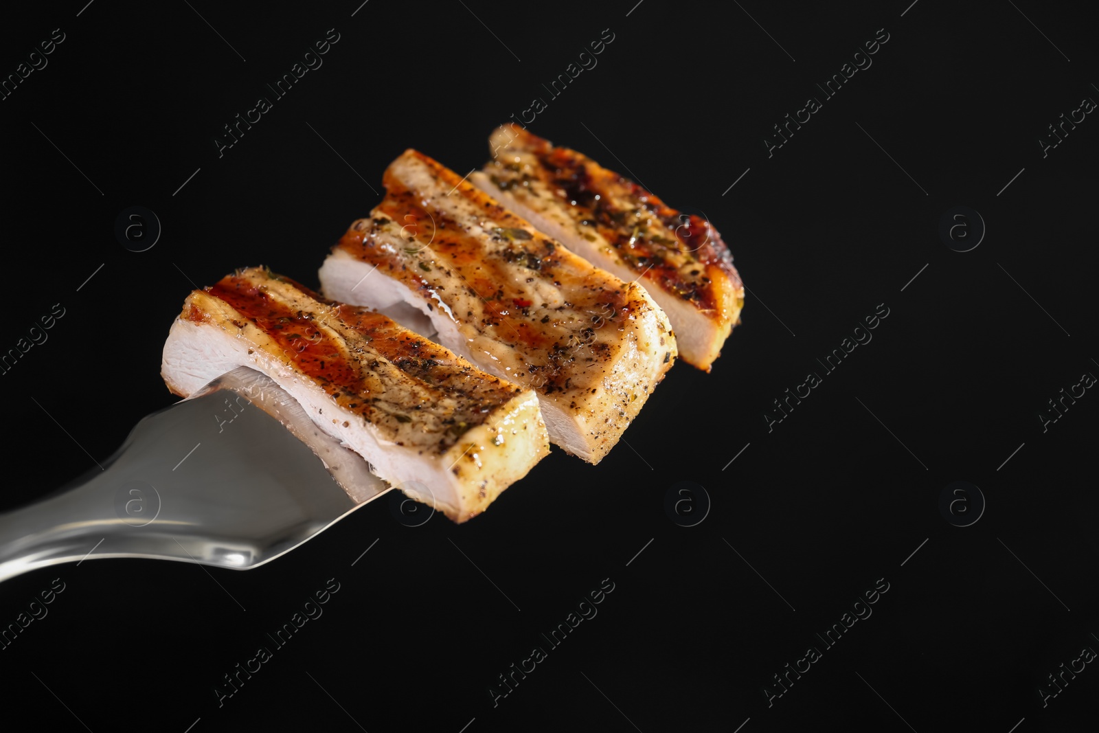 Photo of Meat fork with pieces of delicious grilled pork steak against black background, space for text