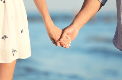 Photo of Happy young couple holding hands at beach on sunny day, closeup