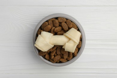 Dry dog food and treat (knotted chew bone) on white wooden floor, top view