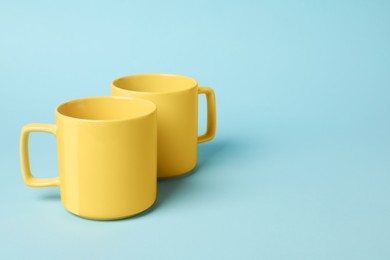 Photo of Two yellow ceramic mugs on light blue background, space for text