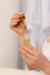 Photo of Woman with bottle of essential oil on blurred background, closeup