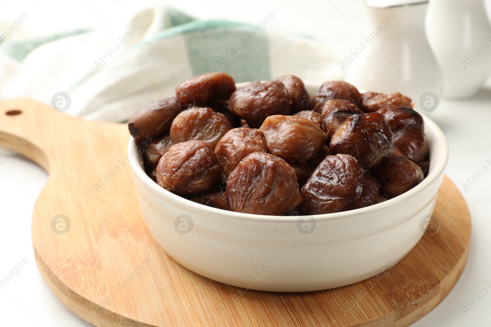 Photo of Roasted edible sweet chestnuts in bowl on white table, closeup