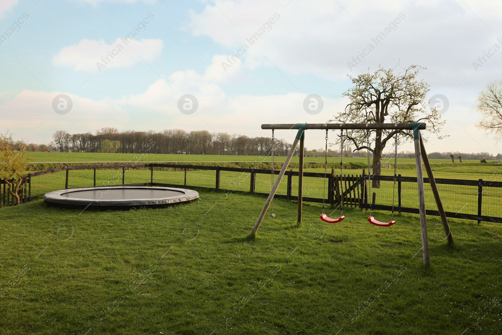 Photo of Wooden swings and trampoline on green lawn outdoors