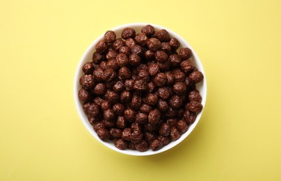 Photo of Chocolate cereal balls in bowl on yellow table, top view