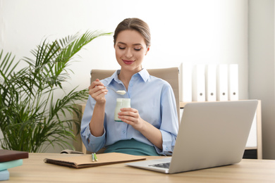 Young attractive woman with tasty yogurt at table in office