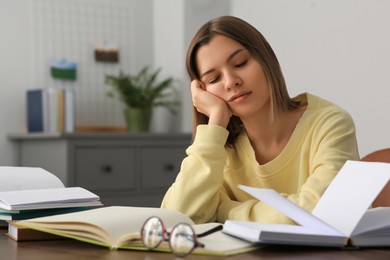 Photo of Young tired woman studying at wooden table in room