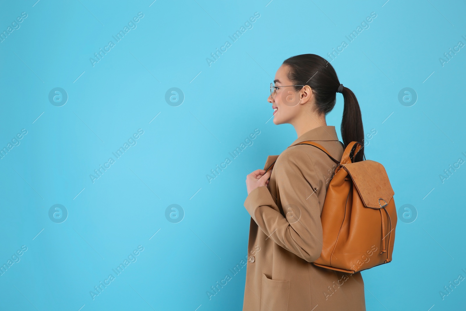 Photo of Beautiful young woman with stylish leather backpack on turquoise background. Space for text