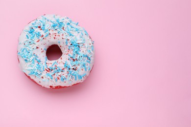 Photo of Glazed donut decorated with sprinkles on pink background, top view. Space for text. Tasty confectionery