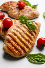 Photo of Tasty grilled chicken fillets with cherry tomatoes and green basil on light grey table, closeup