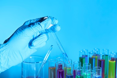 Photo of Scientist dripping liquid from pipette into test tube on light blue background, closeup