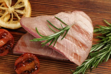Photo of Pieces of delicious tuna steak with rosemary, tomato and lemon on wooden board, closeup
