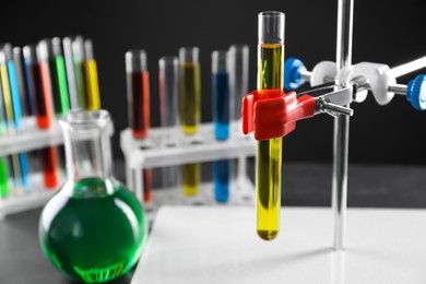 Photo of Retort stand and laboratory glassware with liquids on table against black background, selective focus