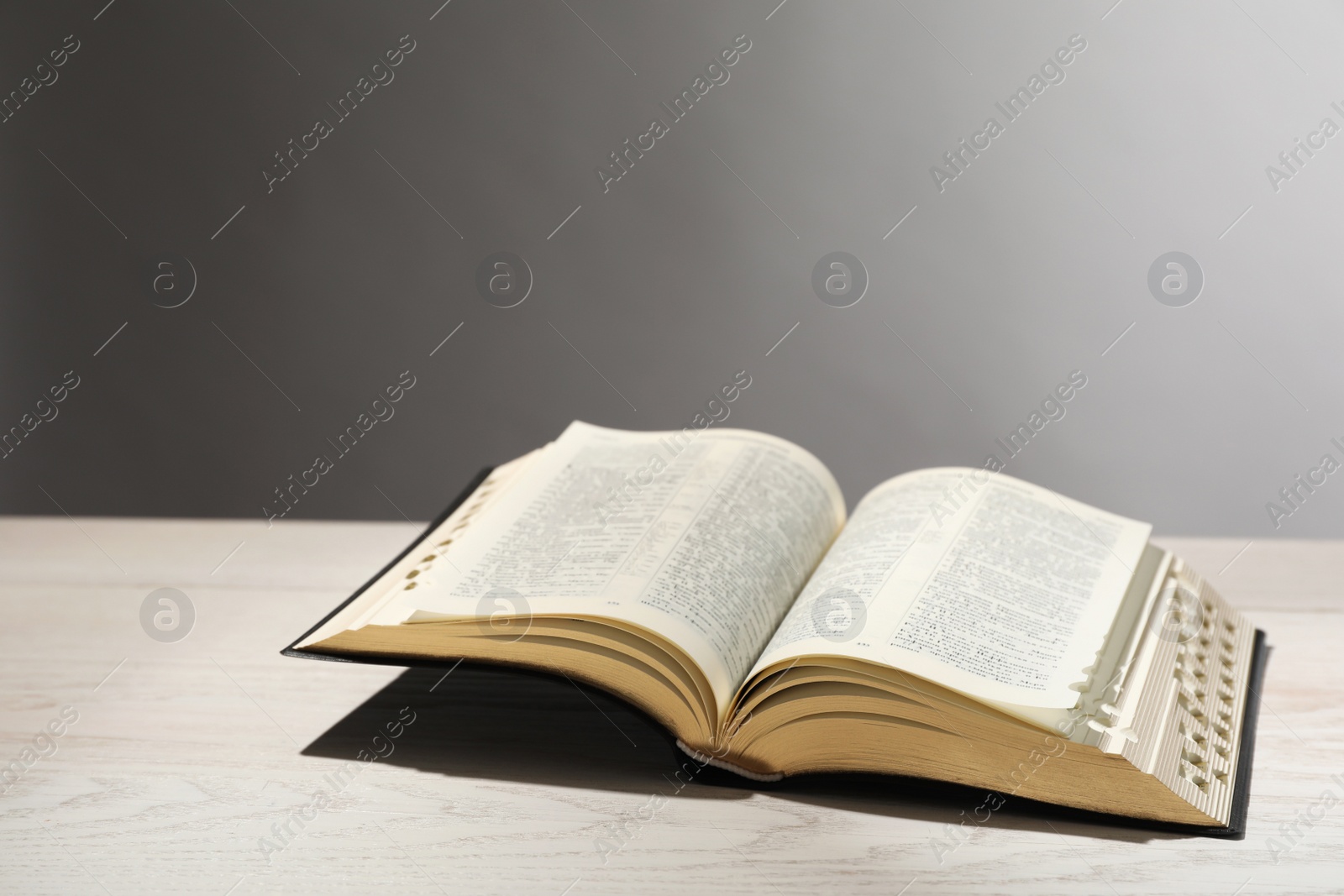 Photo of Open Bible on white wooden table against light grey background. Christian religious book