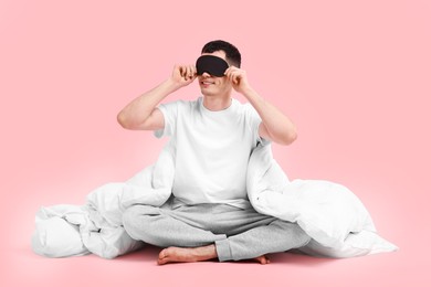 Happy man in pyjama with sleep mask and blanket on pink background