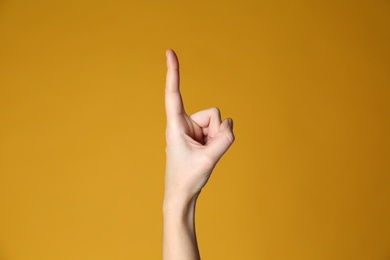 Photo of Woman pointing at something on yellow background, closeup. Finger gesture