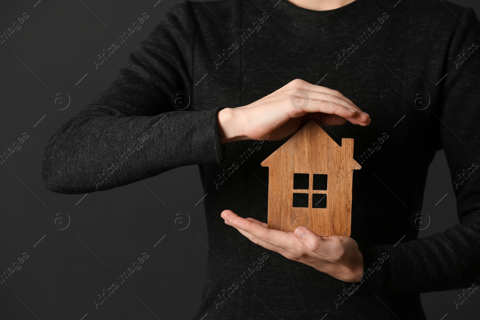 Photo of Woman holding wooden house on dark background, closeup. Home insurance