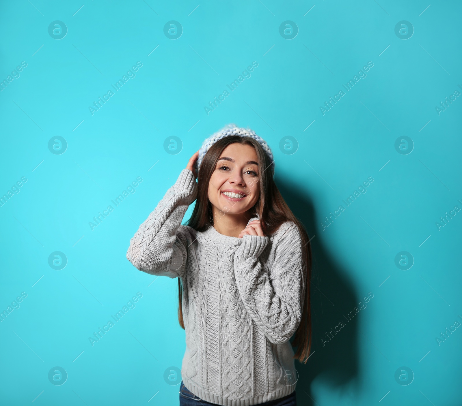 Photo of Beautiful young woman in warm sweater with hat on color background