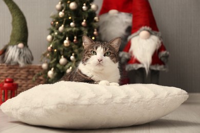 Photo of Cute cat lying on soft pillow near Christmas decor at home. Adorable pet