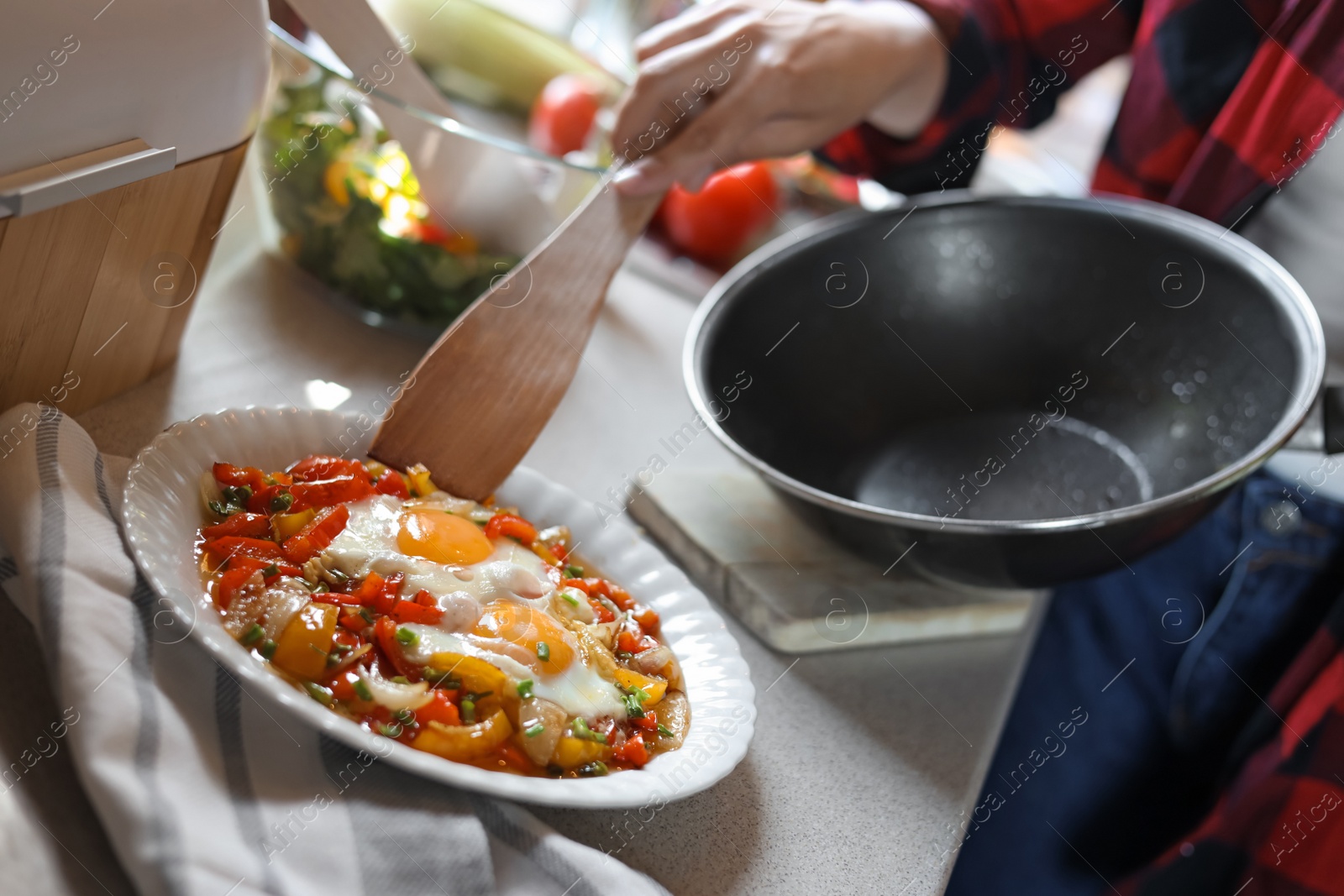 Photo of Woman putting freshly fried eggs with vegetables onto plate in kitchen, closeup