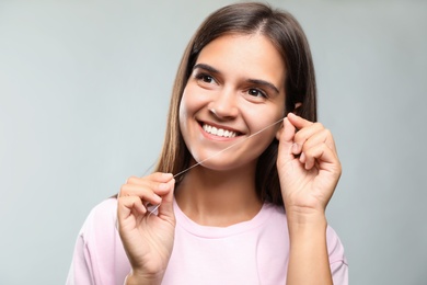 Photo of Young woman flossing her teeth on light grey background. Cosmetic dentistry
