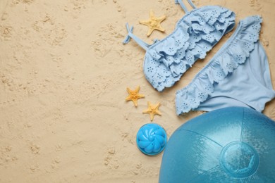 Photo of Light blue beach ball, toy, starfishes and swimsuit on sand, flat lay. Space for text