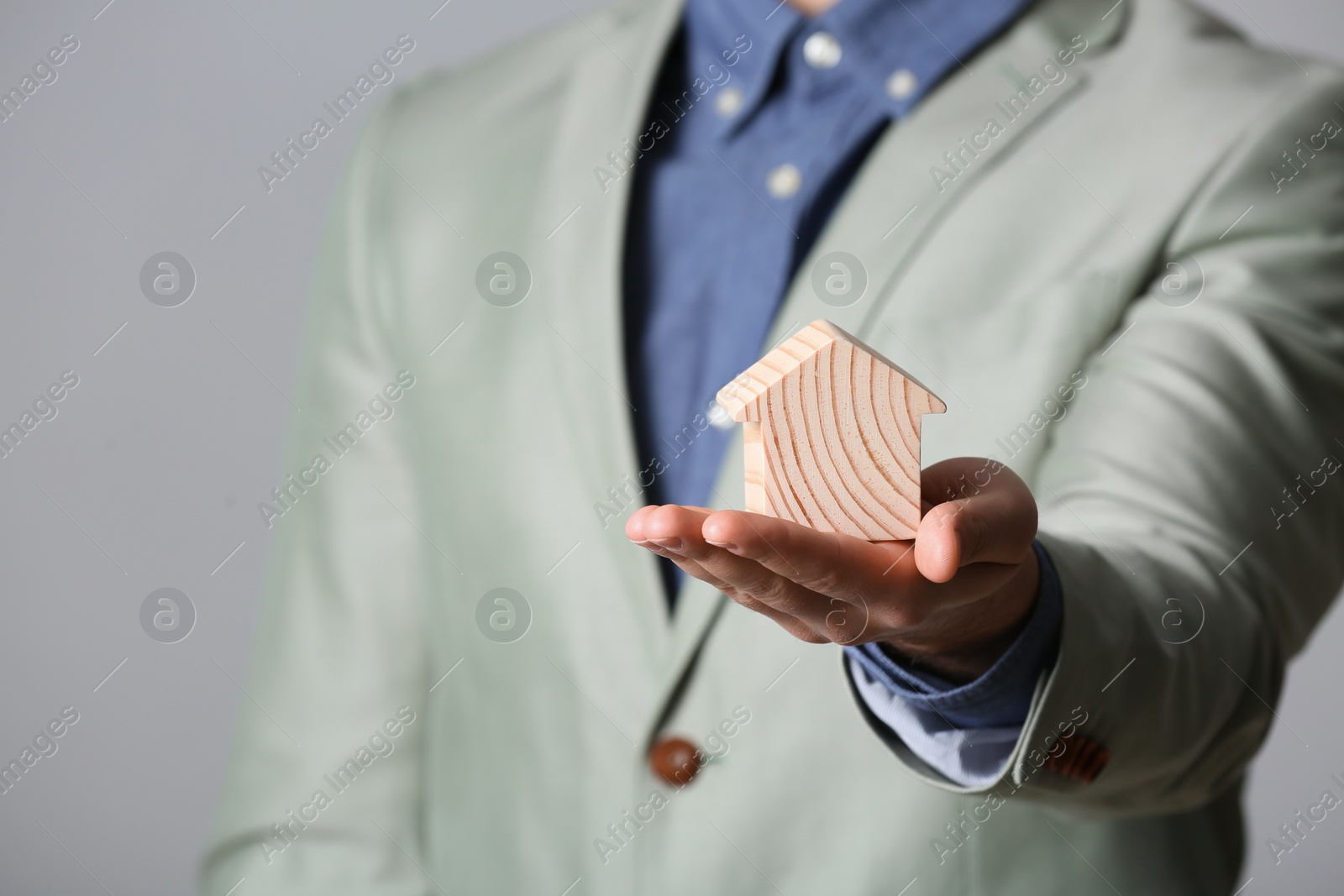 Photo of Male agent holding wooden house on grey background, closeup. Home insurance