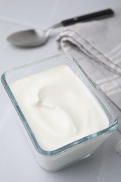 Delicious natural yogurt in glass bowl on white table, closeup