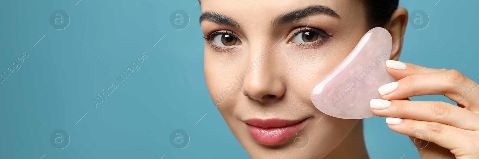 Image of Beautiful young woman doing facial massage with gua sha tool on blue background , space for text. Banner design