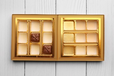 Photo of Partially empty box of chocolate candies on white wooden table, top view