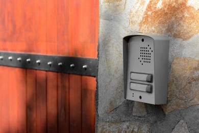 Modern intercom on textured wall with stone fragments outdoors