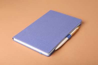 Closed blue notebook and pen on light brown background