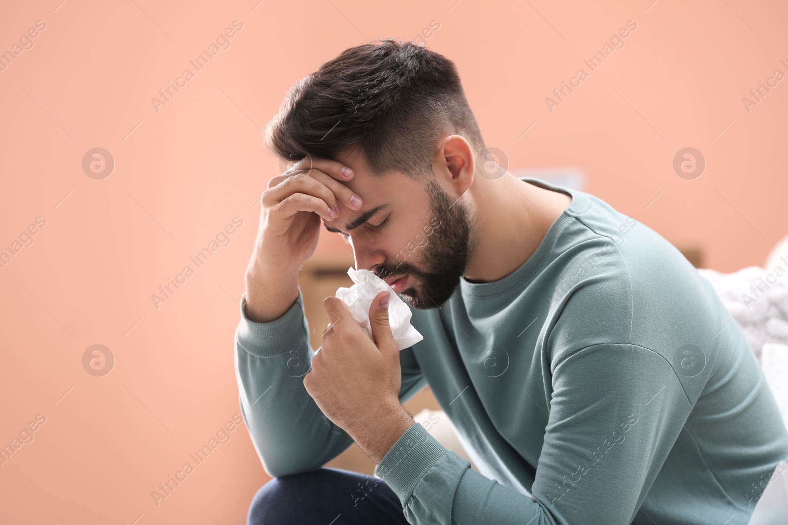 Photo of Young man suffering from runny nose indoors